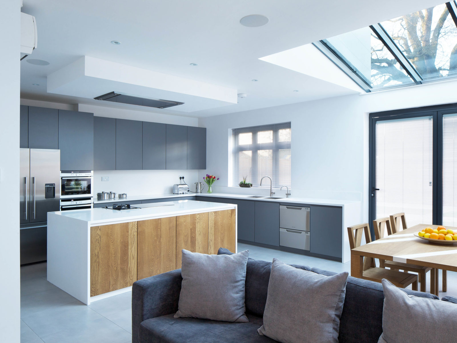 Open plan kitchen with matt grey lacquered doors, Antartica Corian worktop and splashback, solid oak island doors