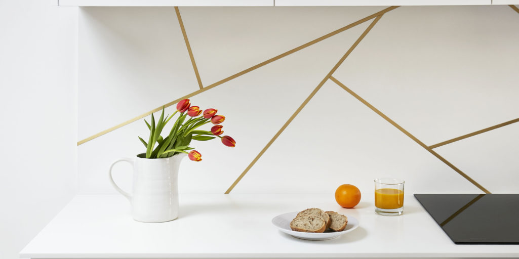 Satin brass inlay splashback design in a white kitchen with Corian worktop