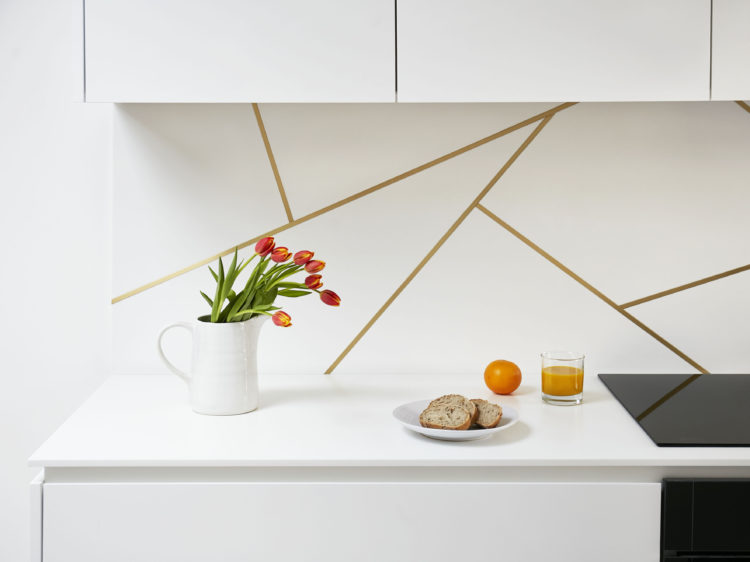 Satin brass inlay splashback design in a white kitchen with Corian worktop