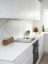 White lacquered handless kitchen with white Corian worktop and satin brass inlay splashback design